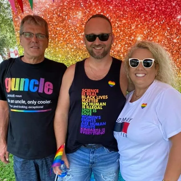 Three friends smiling in front of a rainbow glitter backdrop.