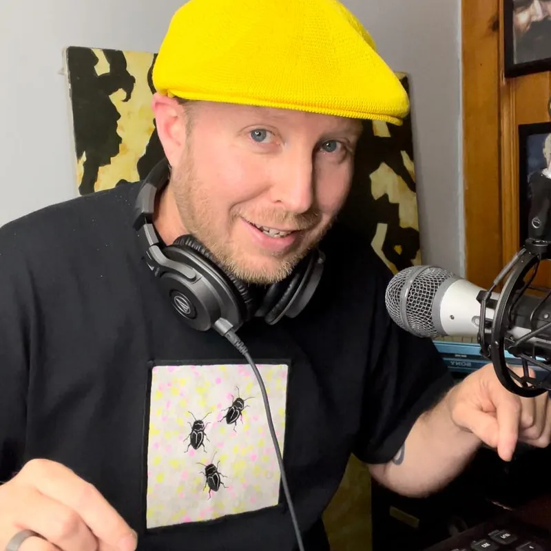 A podcaster in a yellow cap and headphones at a microphone.