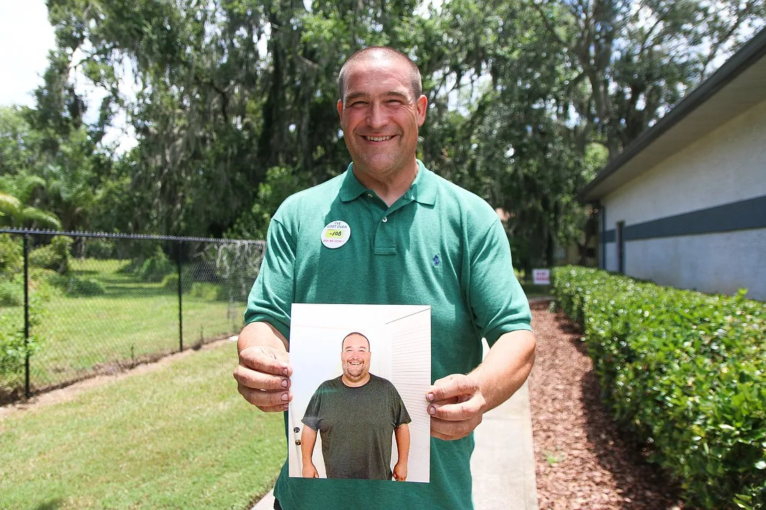 Mike, in a green polo, holds up a photo of himself from before he lost the weight.