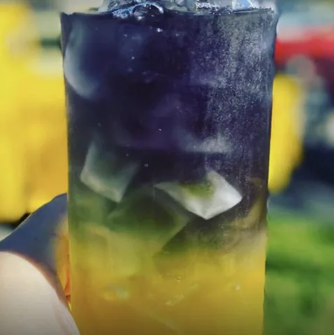 A layered Blue Lagoon Bay power tea, yellow at the bottom and deep blue-purple at the top, full of ice.